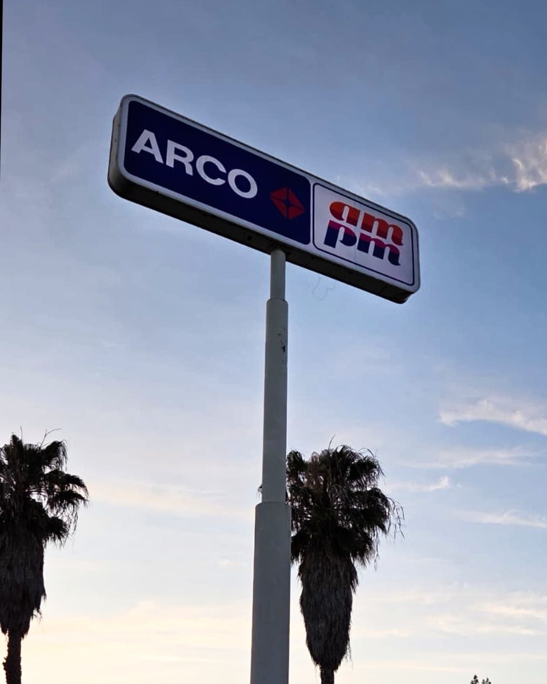 ARCO gas station sign on a tall pole against the evening sky, with palm trees below