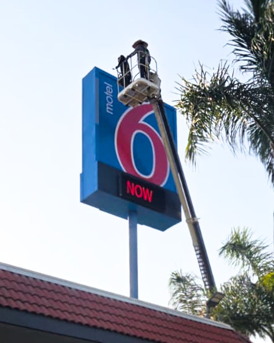 A worker on a lift is repairing a Motel 6 sign with a blue sky
