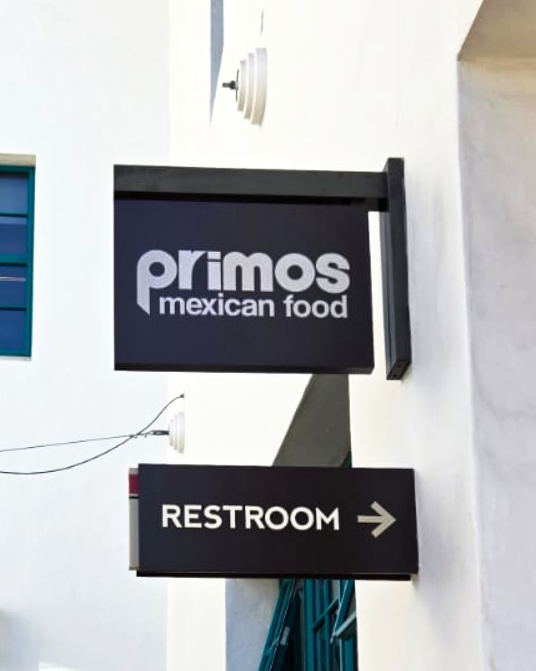 Primos Mexican Food sign above a black restroom sign with a right arrow on a building exterior