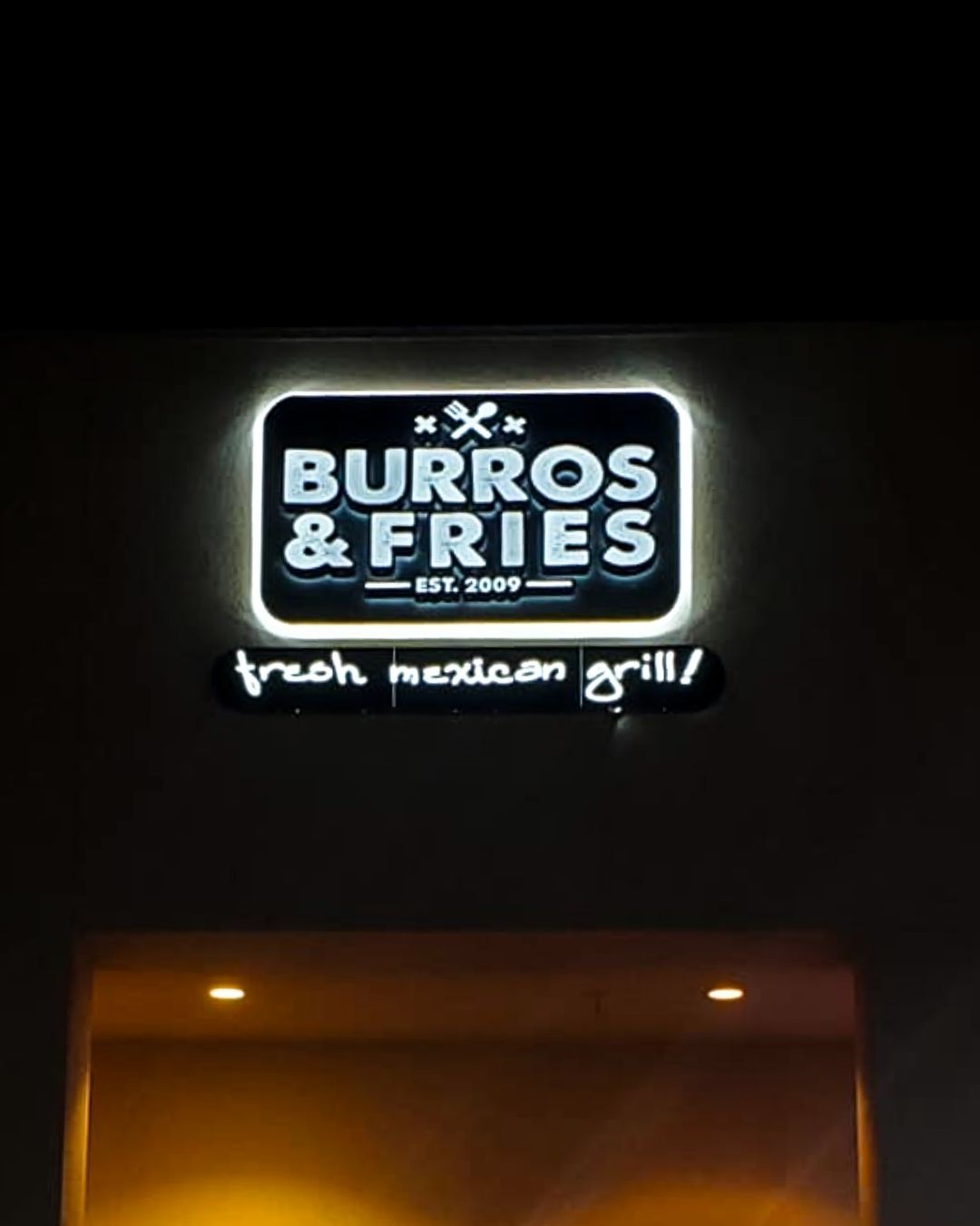 Lit sign for Burros & Fries above a restaurant entrance at night.