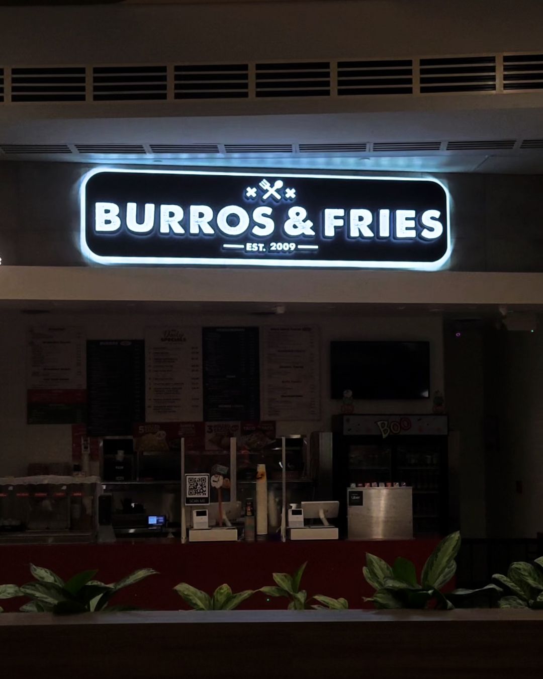 Illuminated BURROS & FRIES restaurant sign above a dark storefront at night