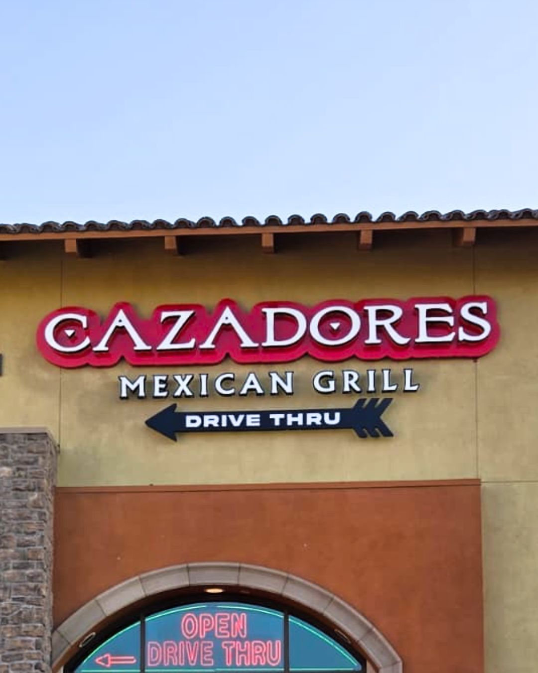 Cazadores Mexican Grill sign on a tan building with a red awning and blue sky above