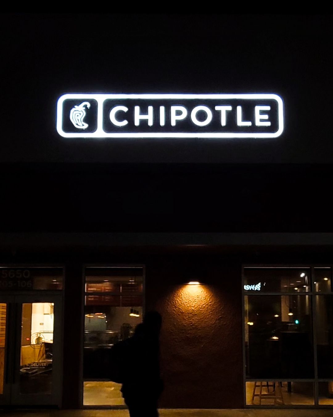 Illuminated Chipotle restaurant sign above a dimly lit storefront at night