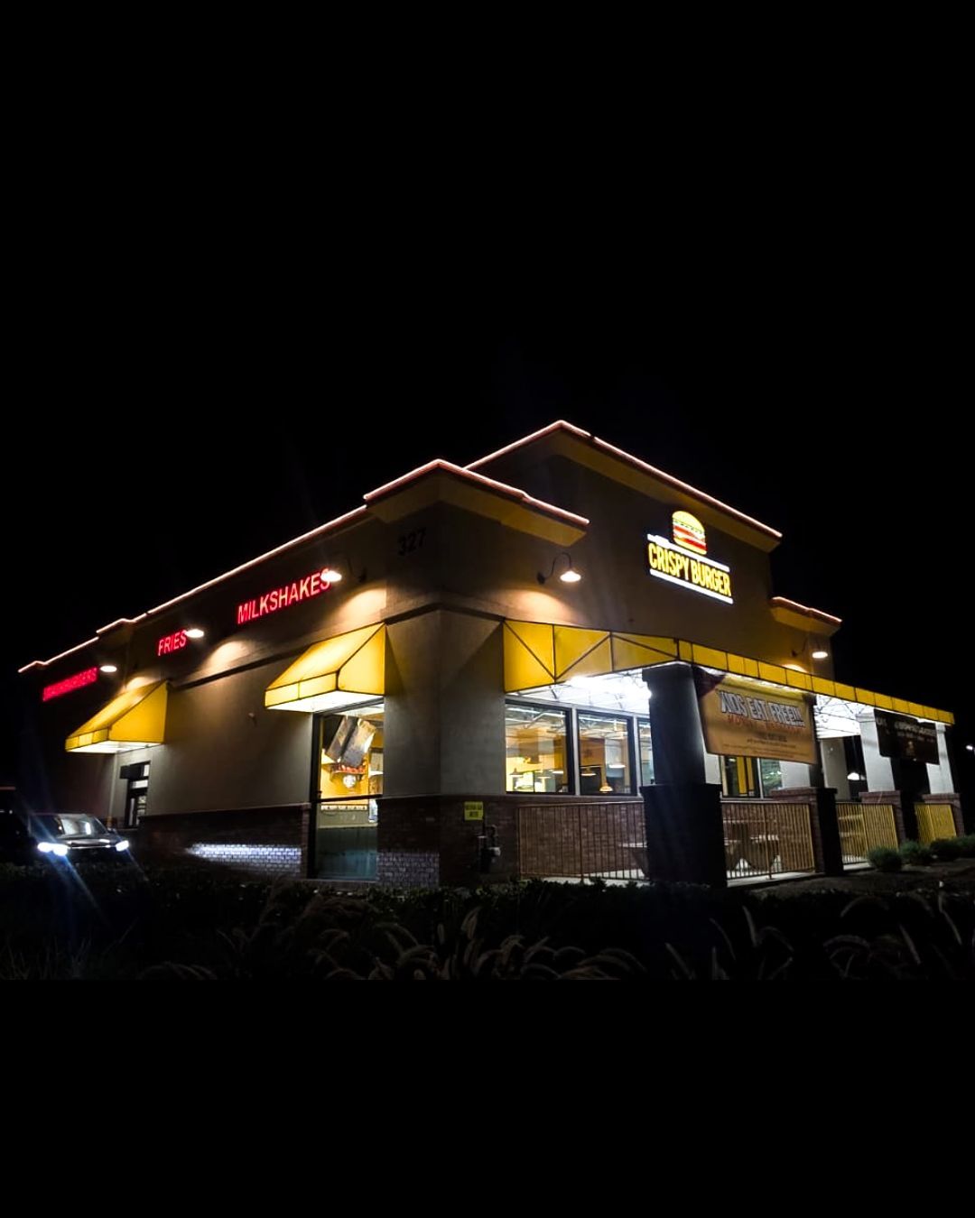 A brightly lit fast-food restaurant at night with yellow awnings and illuminated signs.