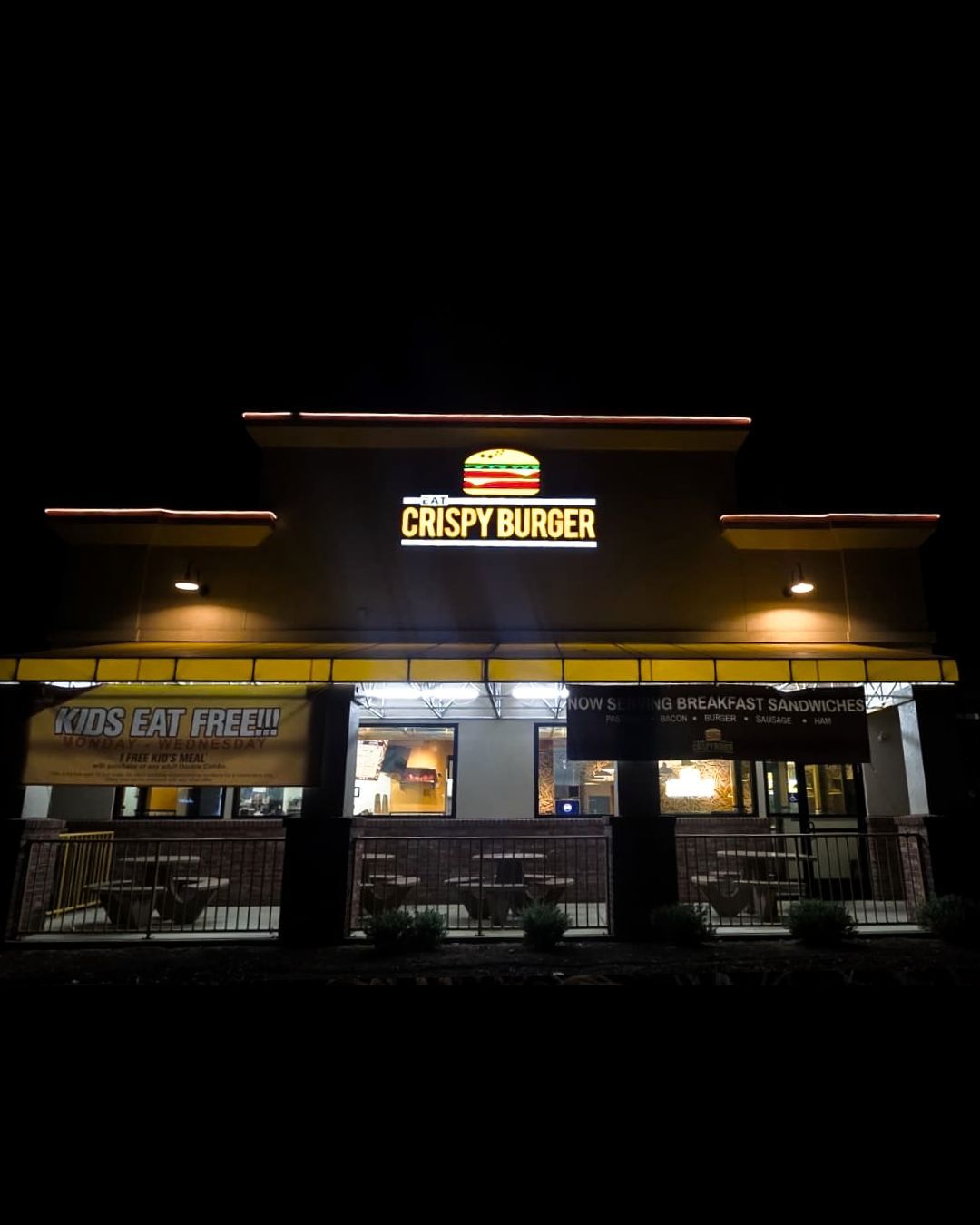 Nighttime exterior of Crispy Burger restaurant with illuminated sign and warm lights above the entrance