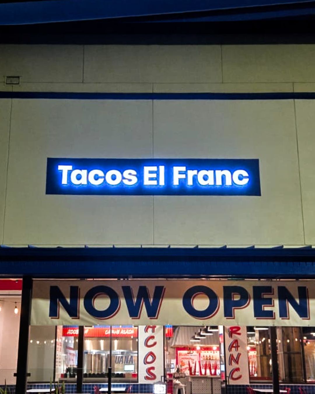 Tacos El Franc storefront at night with bright blue sign and NOW OPEN banner.