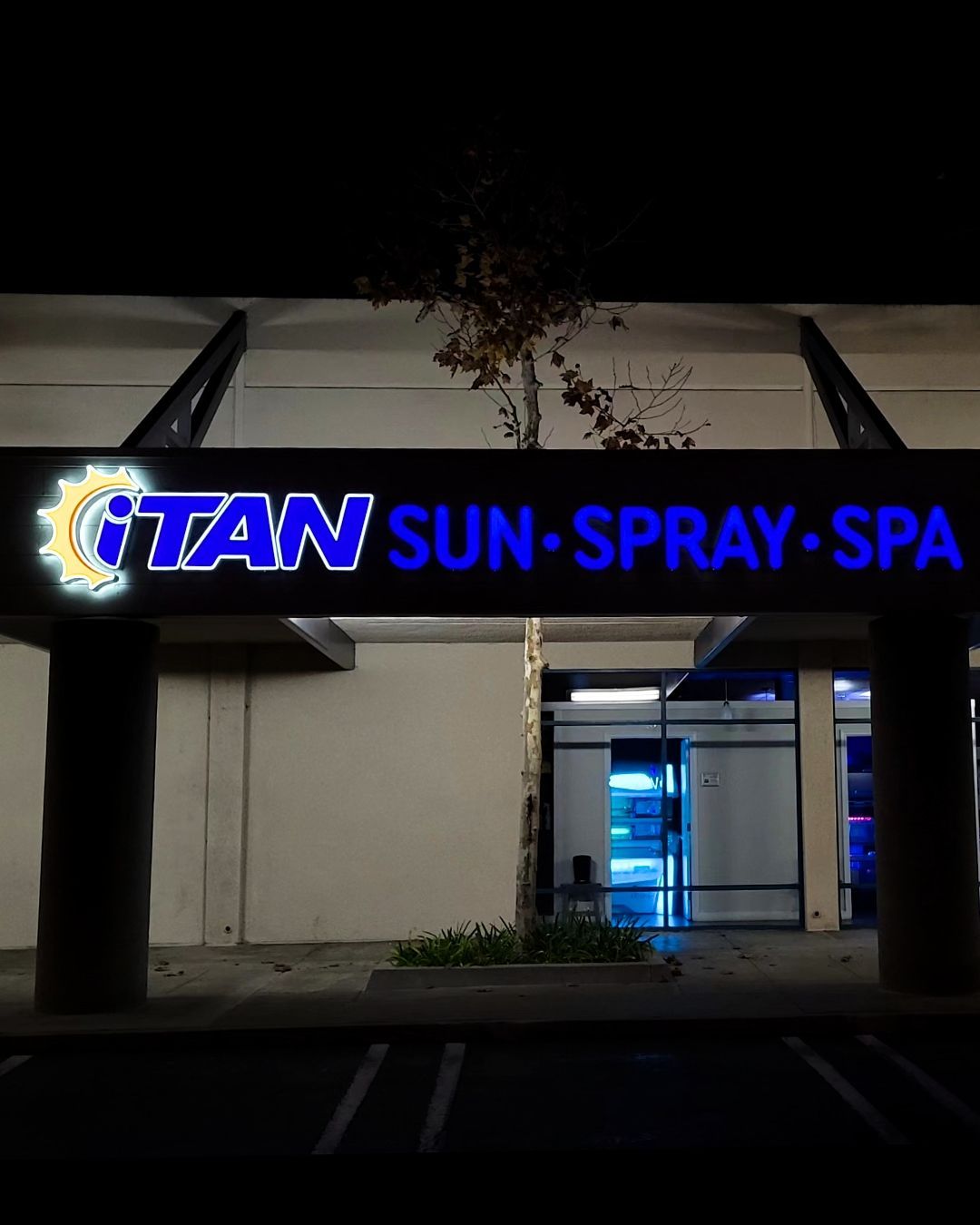 Night exterior of a spa entrance with a blue neon TAN SUN-SPRAY-SPA sign above the doorway.