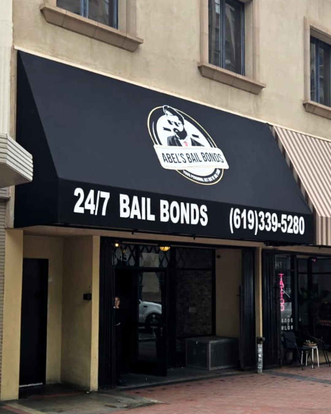 Black awning storefront for 24/7 bail bonds with phone number, on a city sidewalk