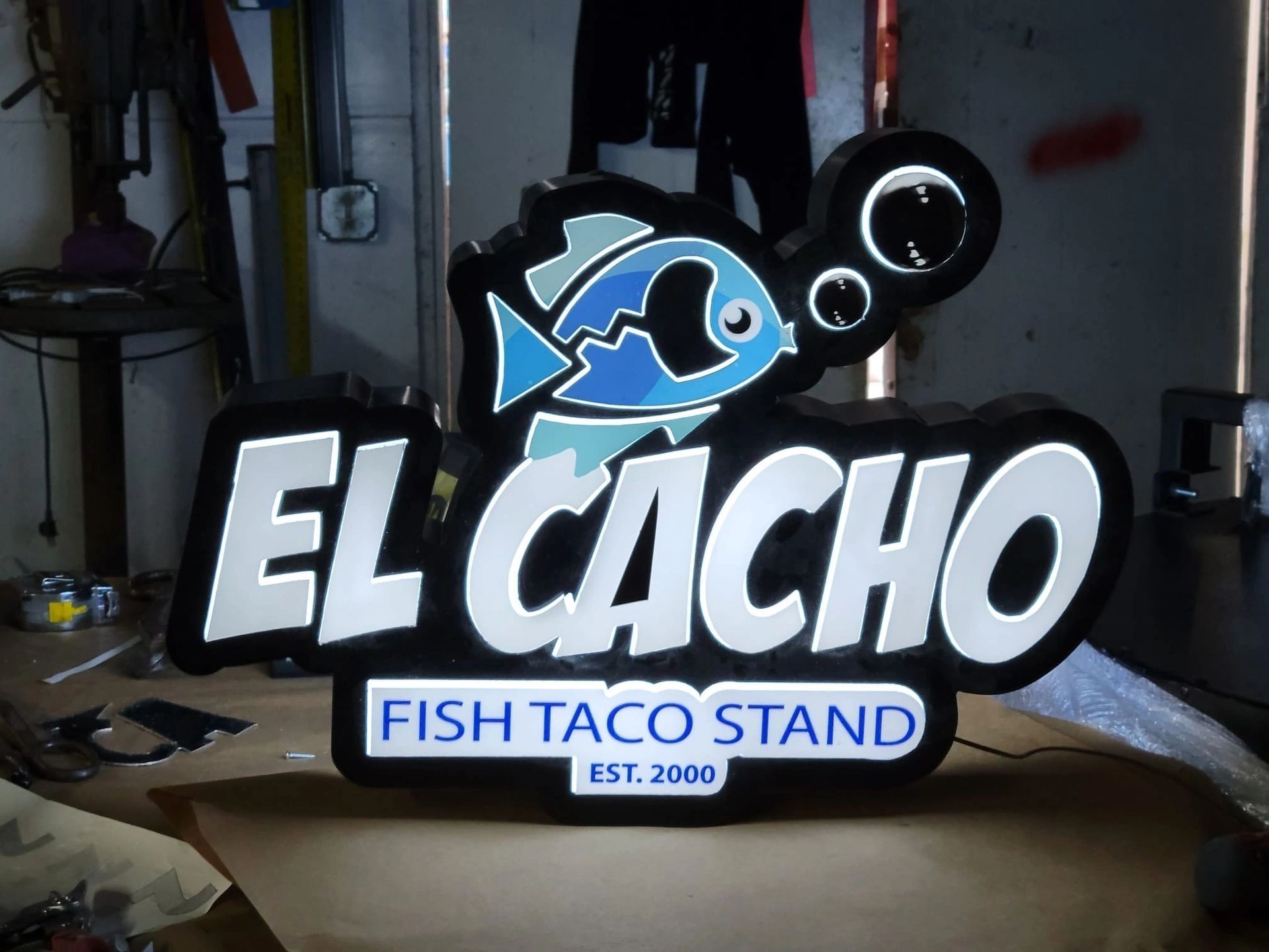 Illuminated El Cacho Fish Taco Stand sign with blue fish logo and white lettering