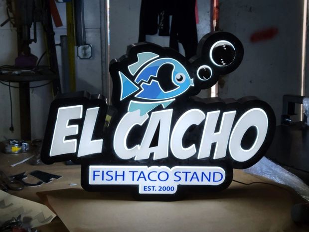 EL CACHO Fish Taco Stand sign with blue fish logo and white lettering, lit against a dark background
