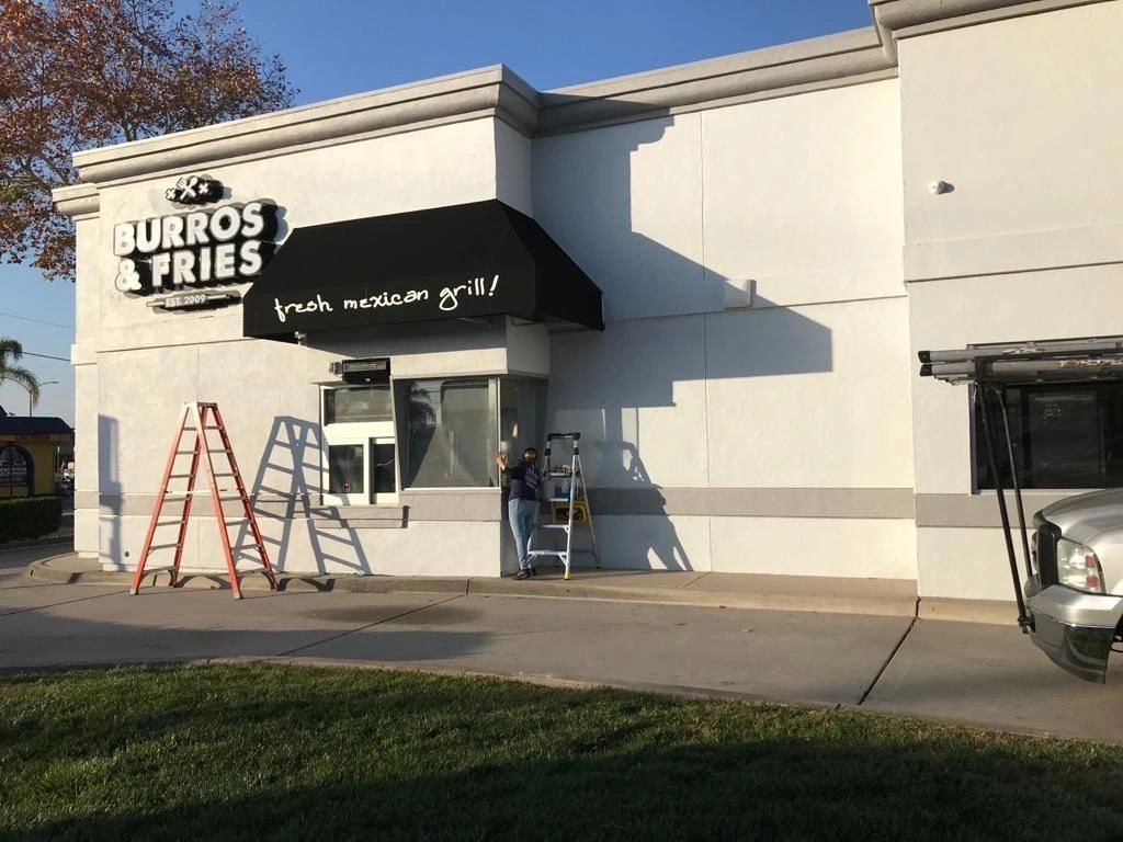 Turros Fries storefront with ladders and workers under a black awning, viewed from the sidewalk.