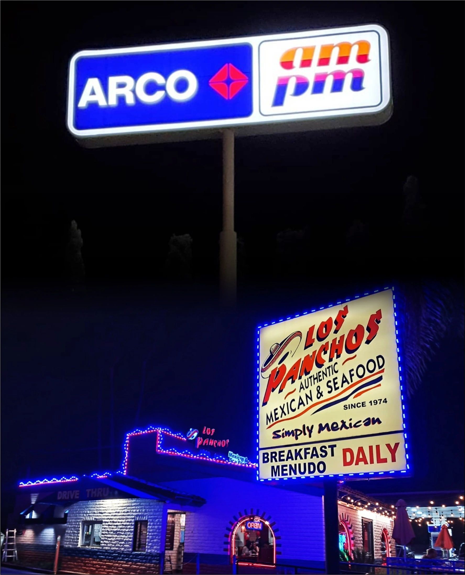 Nighttime view of an ARCO gas station sign and a neon-lit restaurant exterior with a seafood menu board.