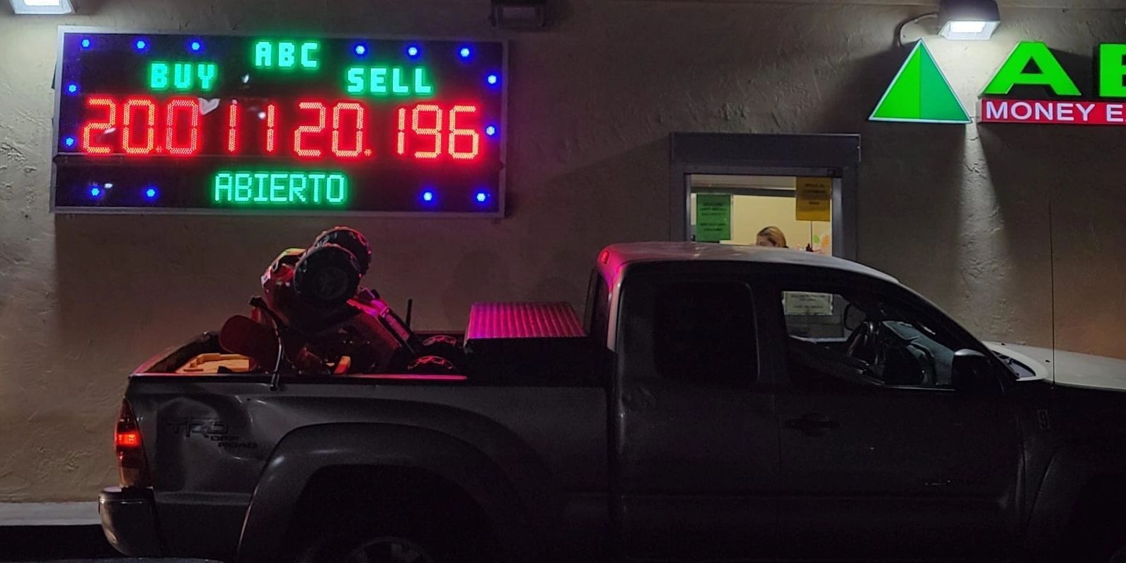Night scene of a black pickup truck outside a neon-lit currency exchange booth.