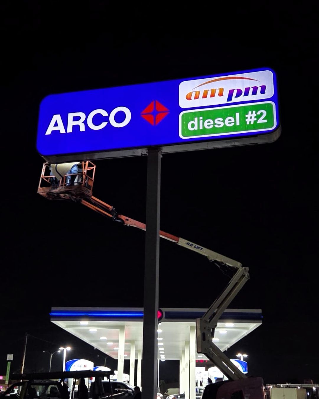 ARCO gas station sign lit at night, with a worker in a lift replacing the sign panel.