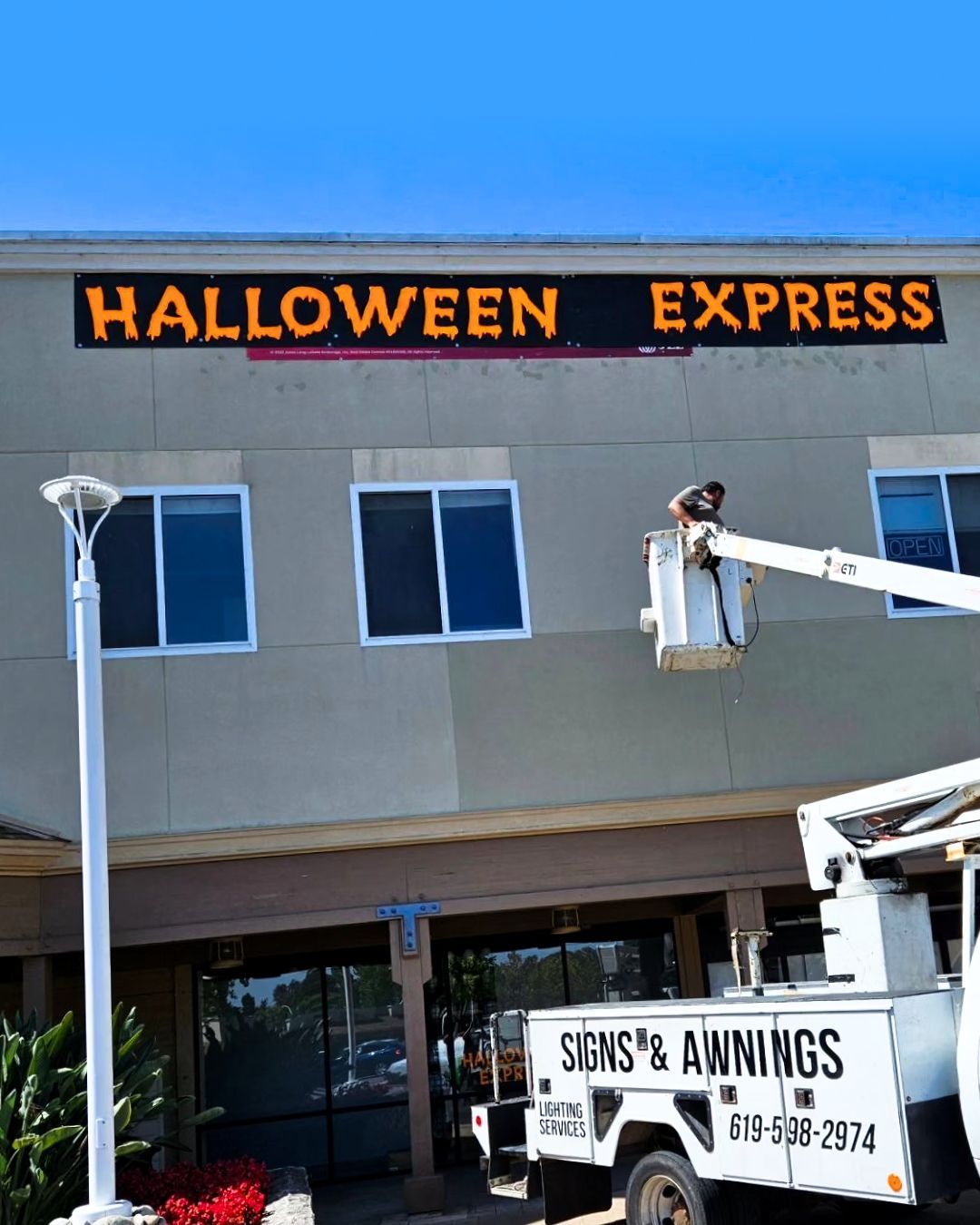Halloween Express storefront sign above a building, with a worker in a lift below.