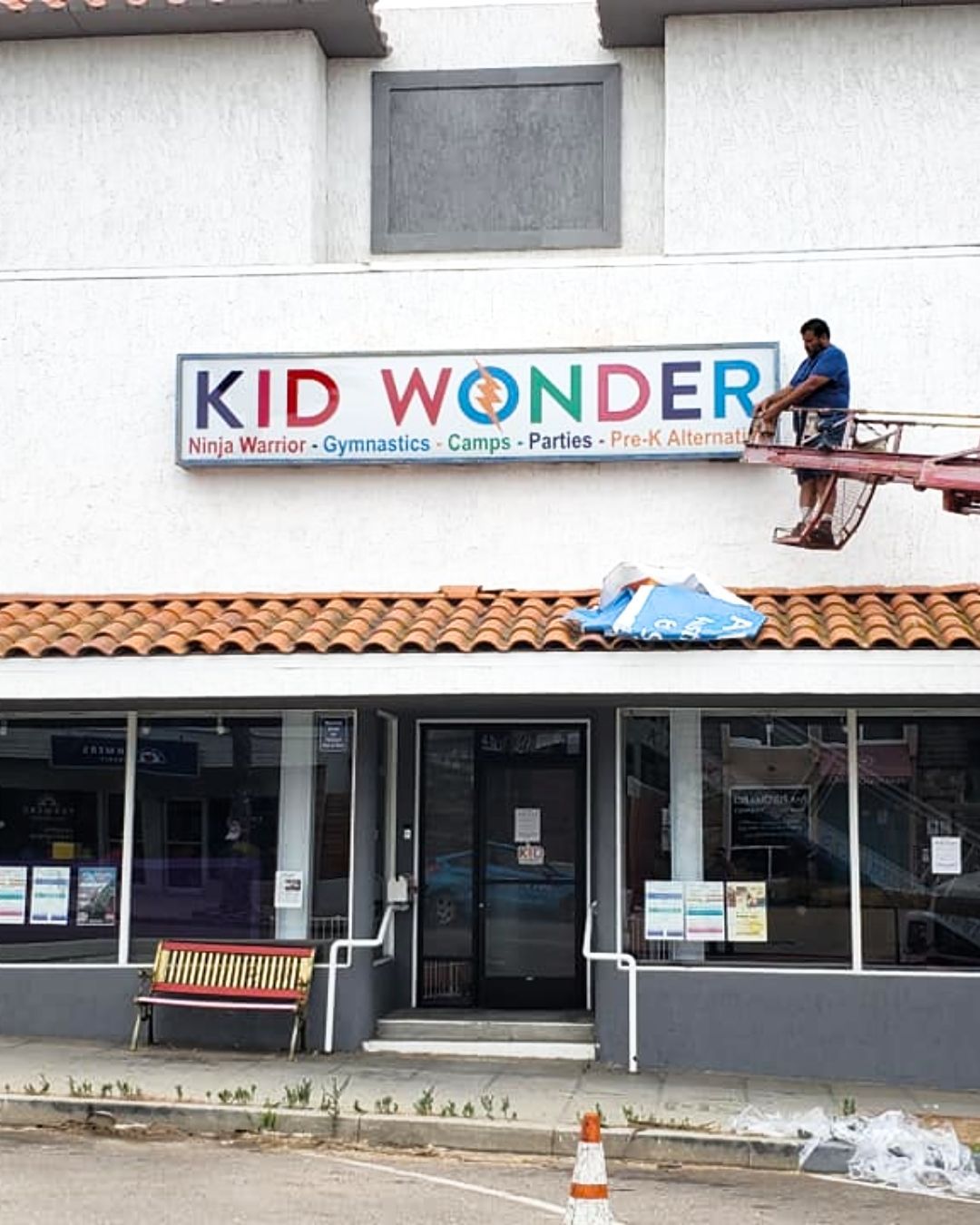 Storefront sign reading KID WONDER, with a worker on the roof above the entrance.