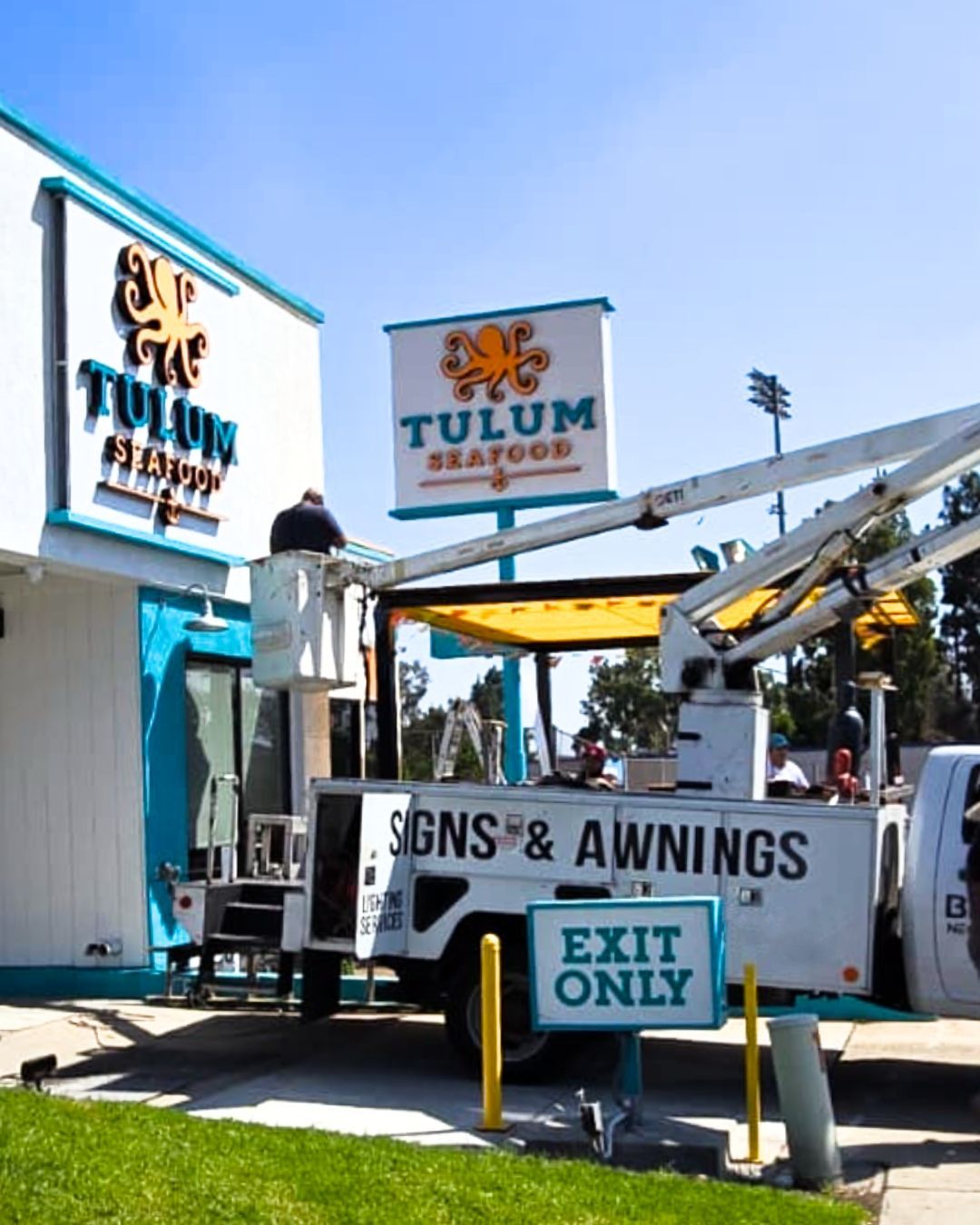 Tulum Sign Shop truck with crane and an EXIT ONLY sign in a bright outdoor yard