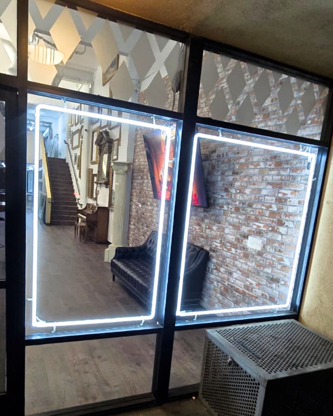 Indoor window view of a narrow stairwell and brick wall, with a lit mirror and small bench below