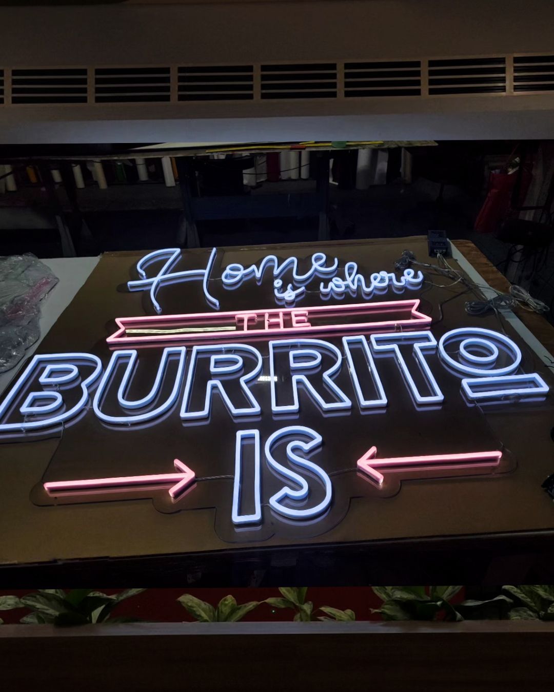 Neon sign on a table reading Home is where BURRITO IS in pink and blue lights.