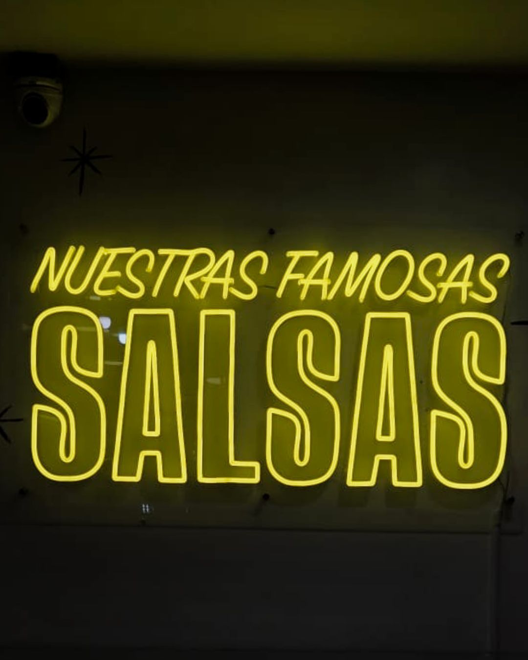 Neon sign reading NUESTRAS FAMOSAS SALSAS in yellow on a dark wall.