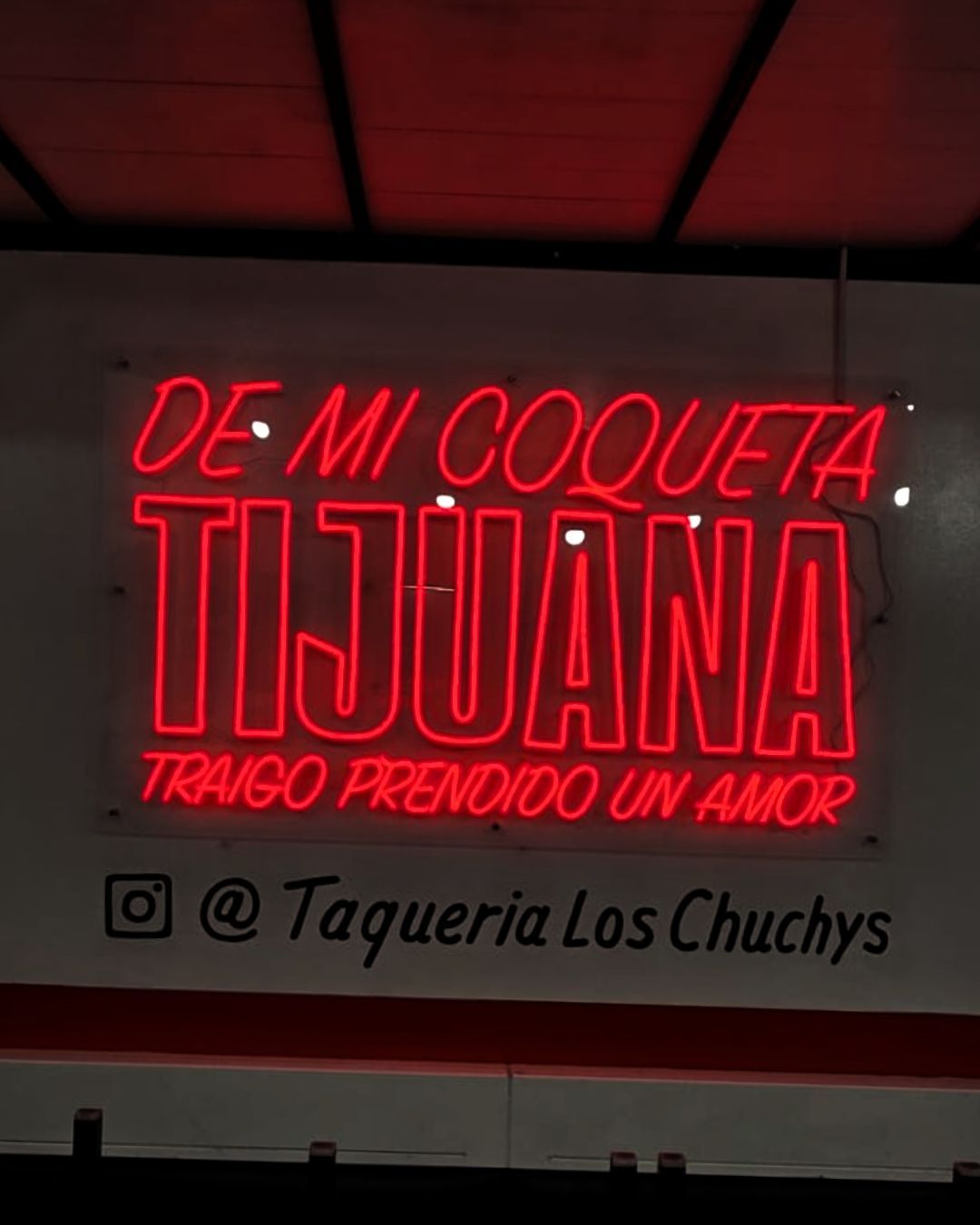 Red neon sign reading DE MI COQUITA TIJUANA with Instagram handle @Taqueria Los Chichys.