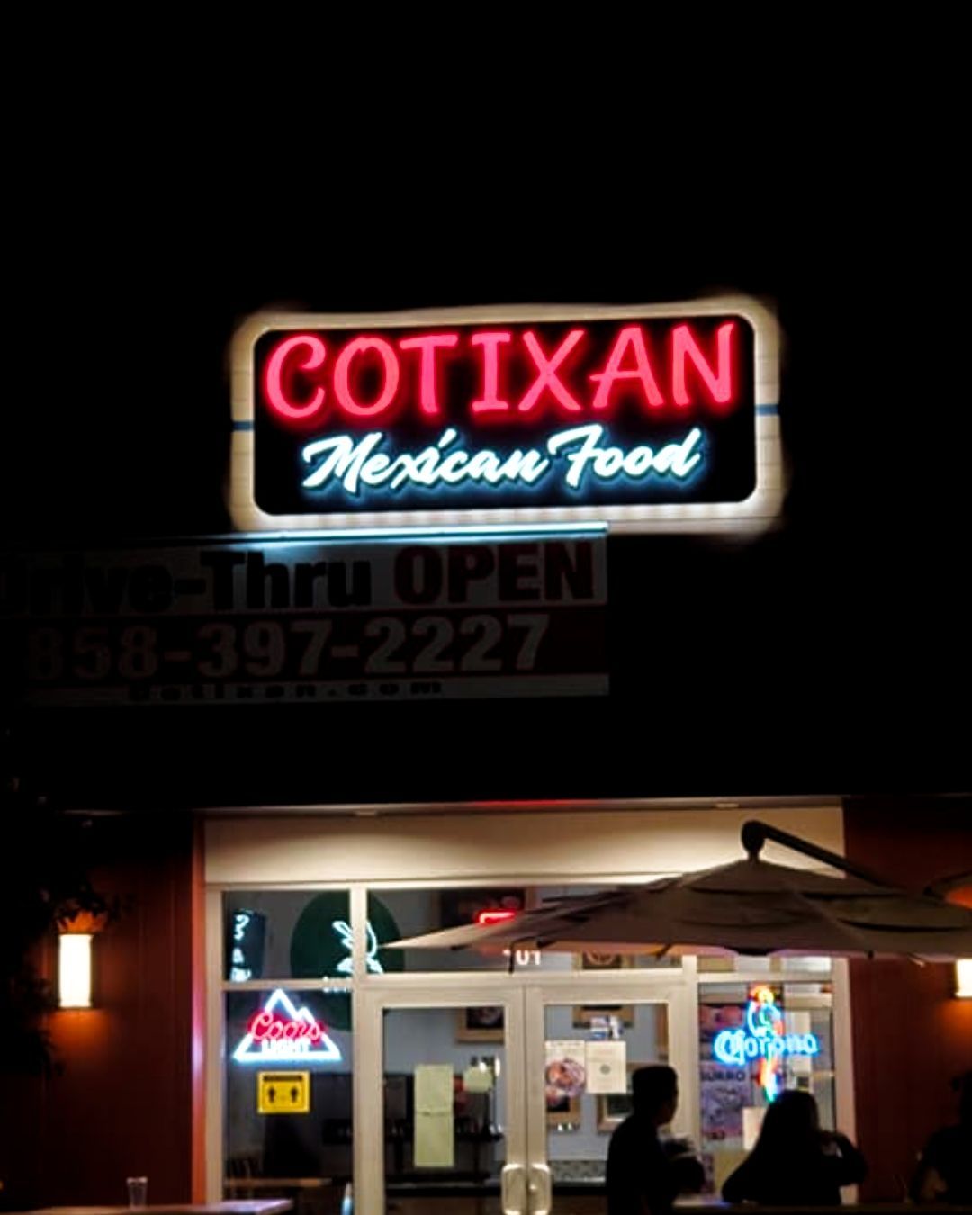 Neon-lit Cotixan Mexican Food restaurant storefront at night with patio seating and customers.