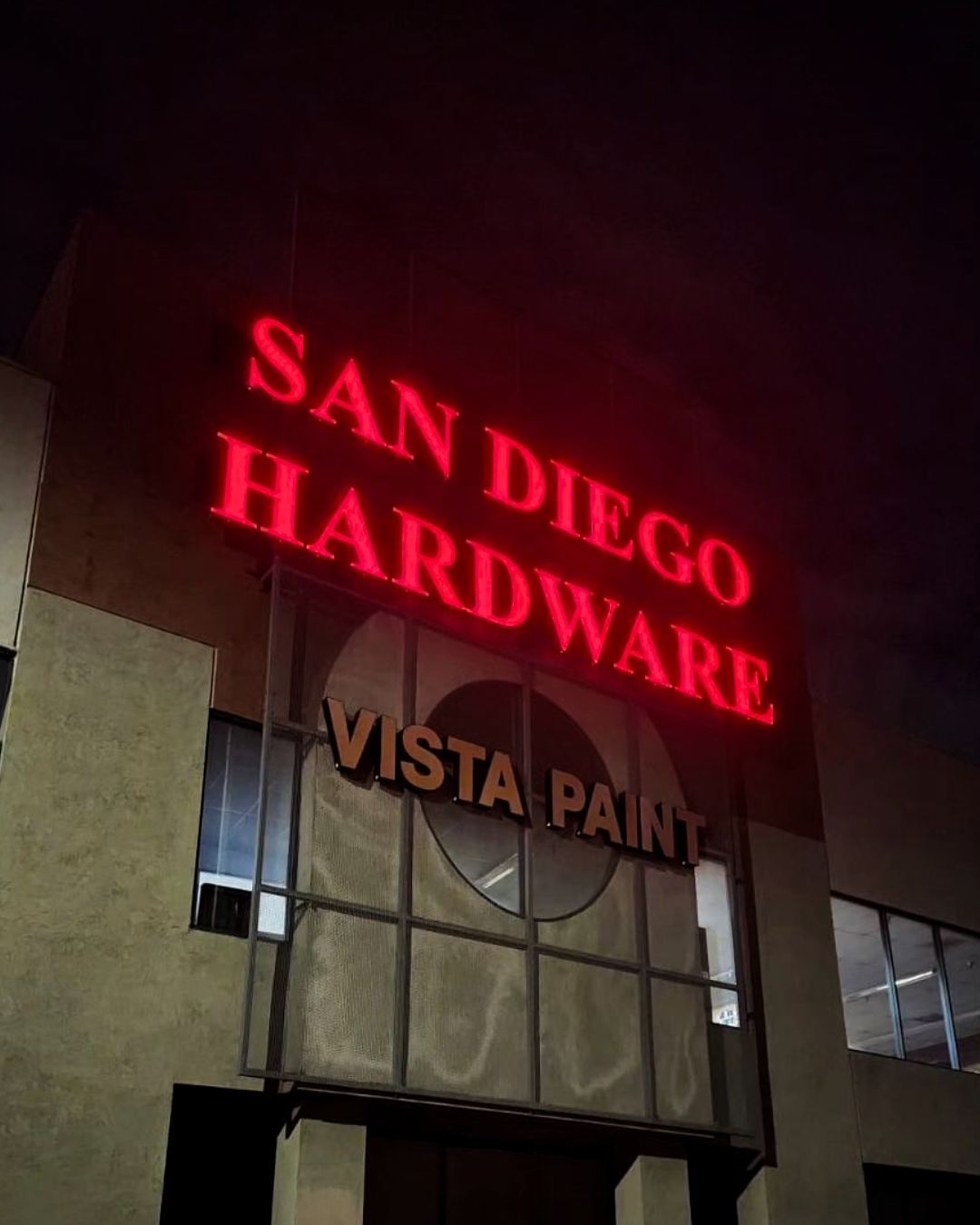 Lit storefront sign reading San Diego Hardware in red and “Vista Paint” below at night
