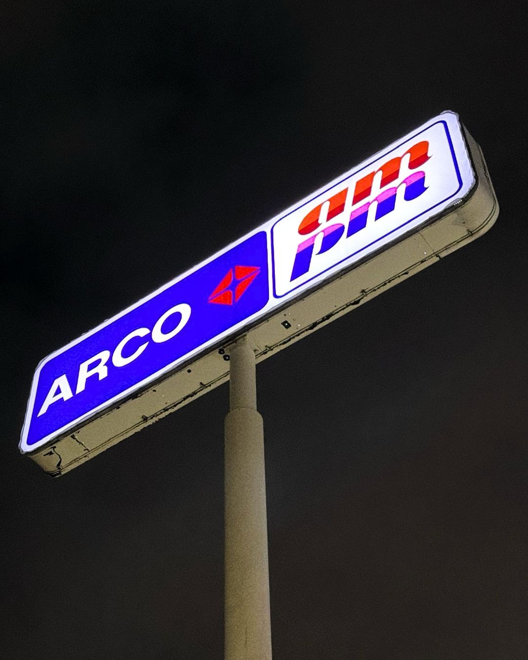 Illuminated ARCO gas station sign with a blue and red logo against a dark night sky