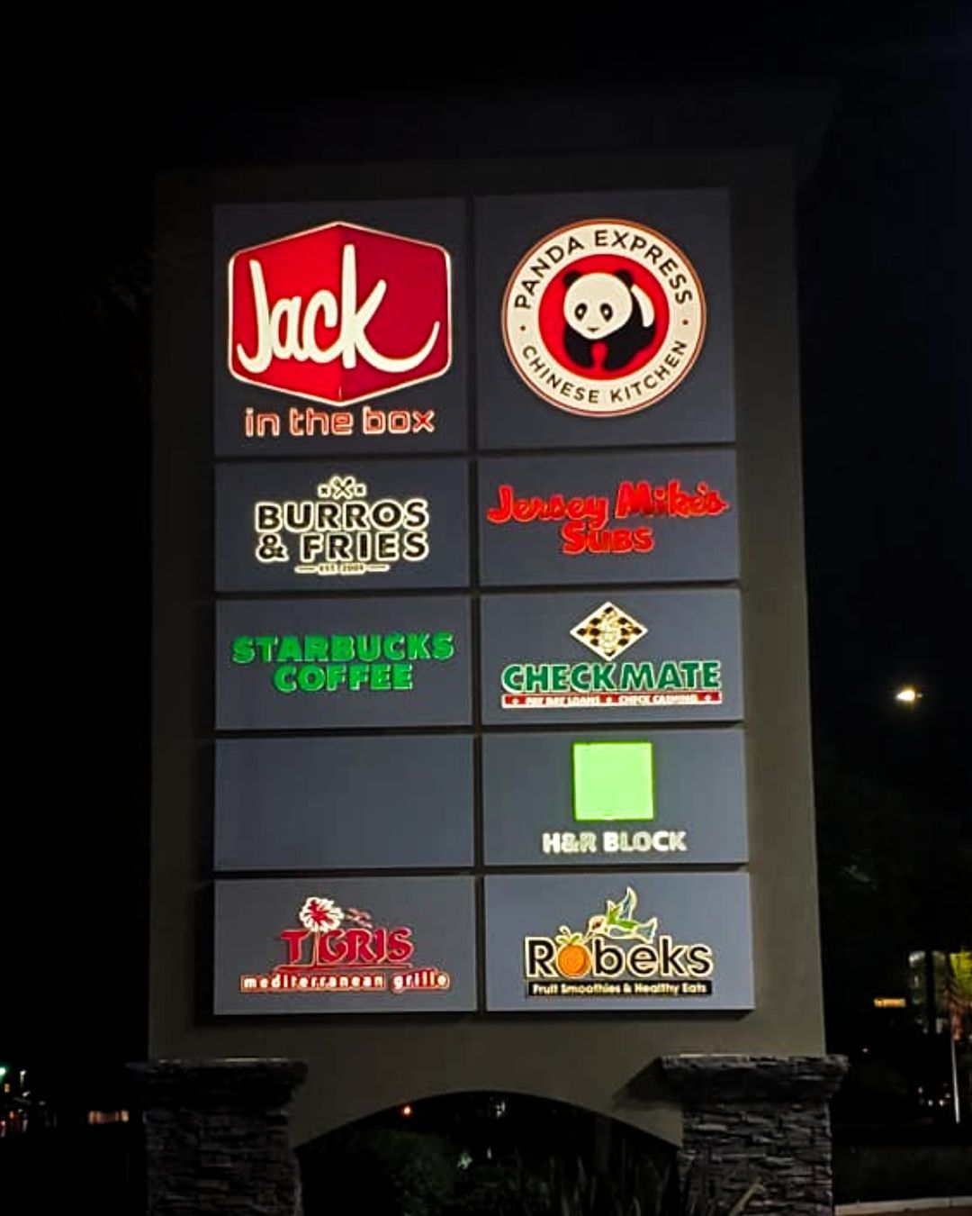 Outdoor sign with multiple restaurant logos, including Jack in the Box and Starbucks Coffee, lit at night
