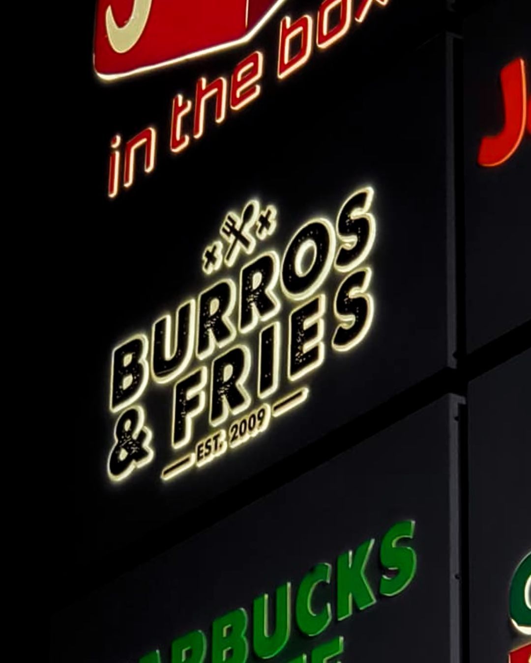 Neon Burros & Fries sign on a dark storefront, with green Starbucks lettering below.