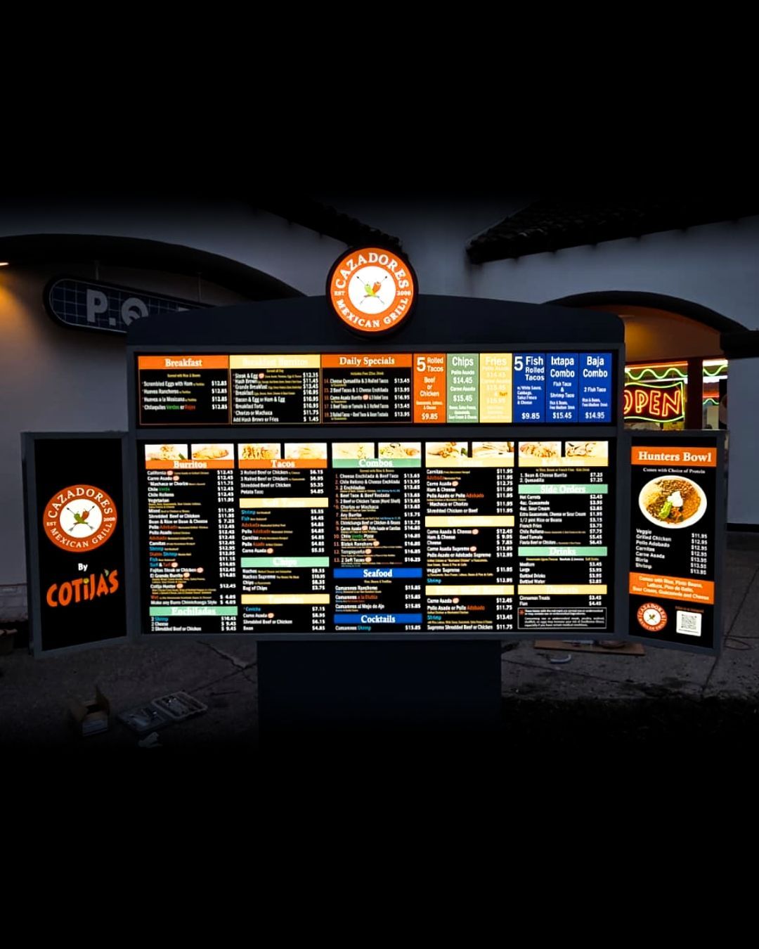 Coffee shop menu boards with orange and blue sections on a dark storefront wall