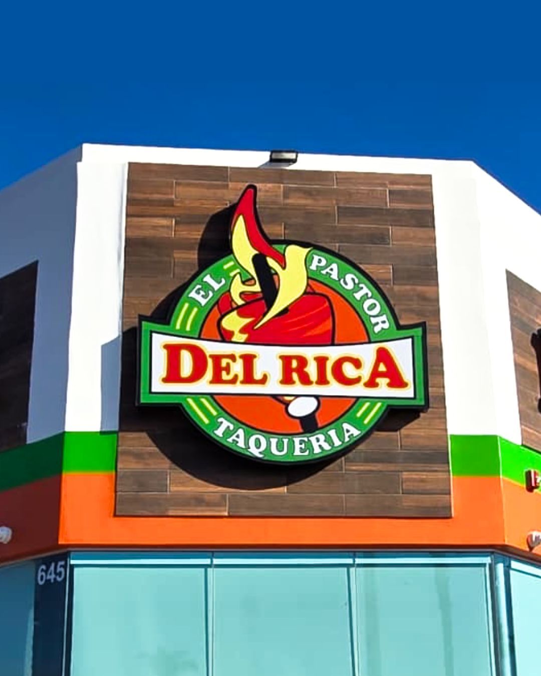 El Rico El Pastor Taqueria sign on a wood panel above a storefront with blue and orange trim
