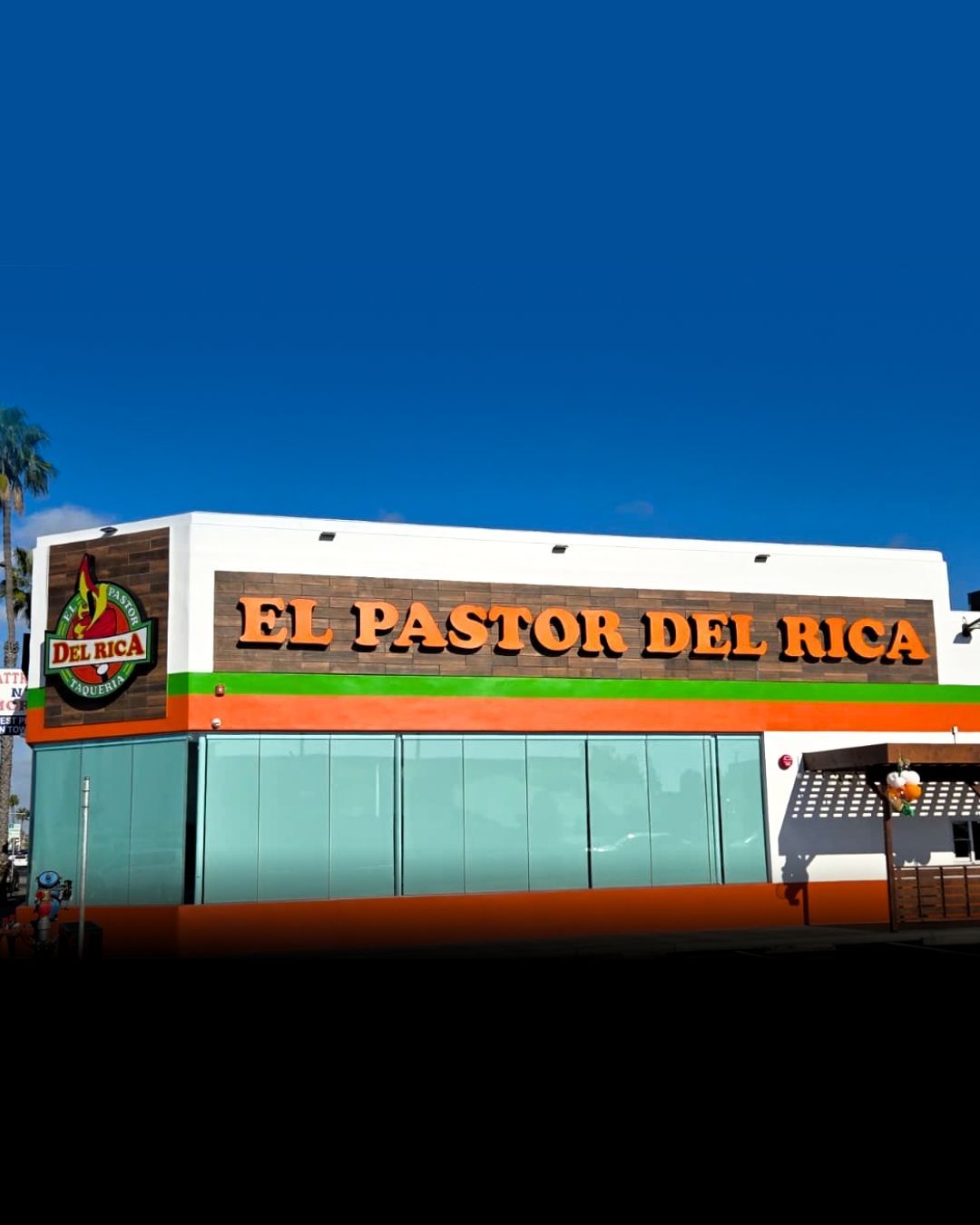 Exterior of El Pastor del Rica restaurant with white facade, orange signage, and blue sky