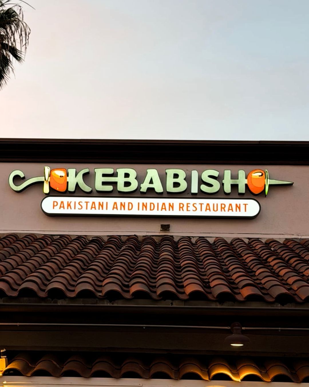 Crisbakebisho restaurant sign above tiled roof at dusk, with Pakistani and Indian Restaurant subtitle