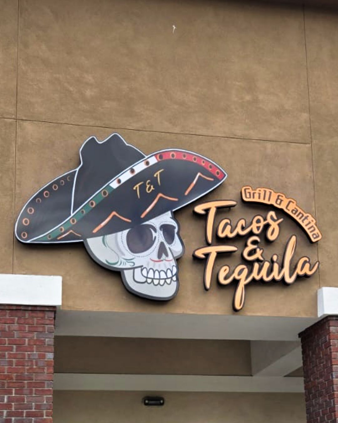Tacos & Tequila storefront sign with a sombrero-topped skull logo and warm orange lettering