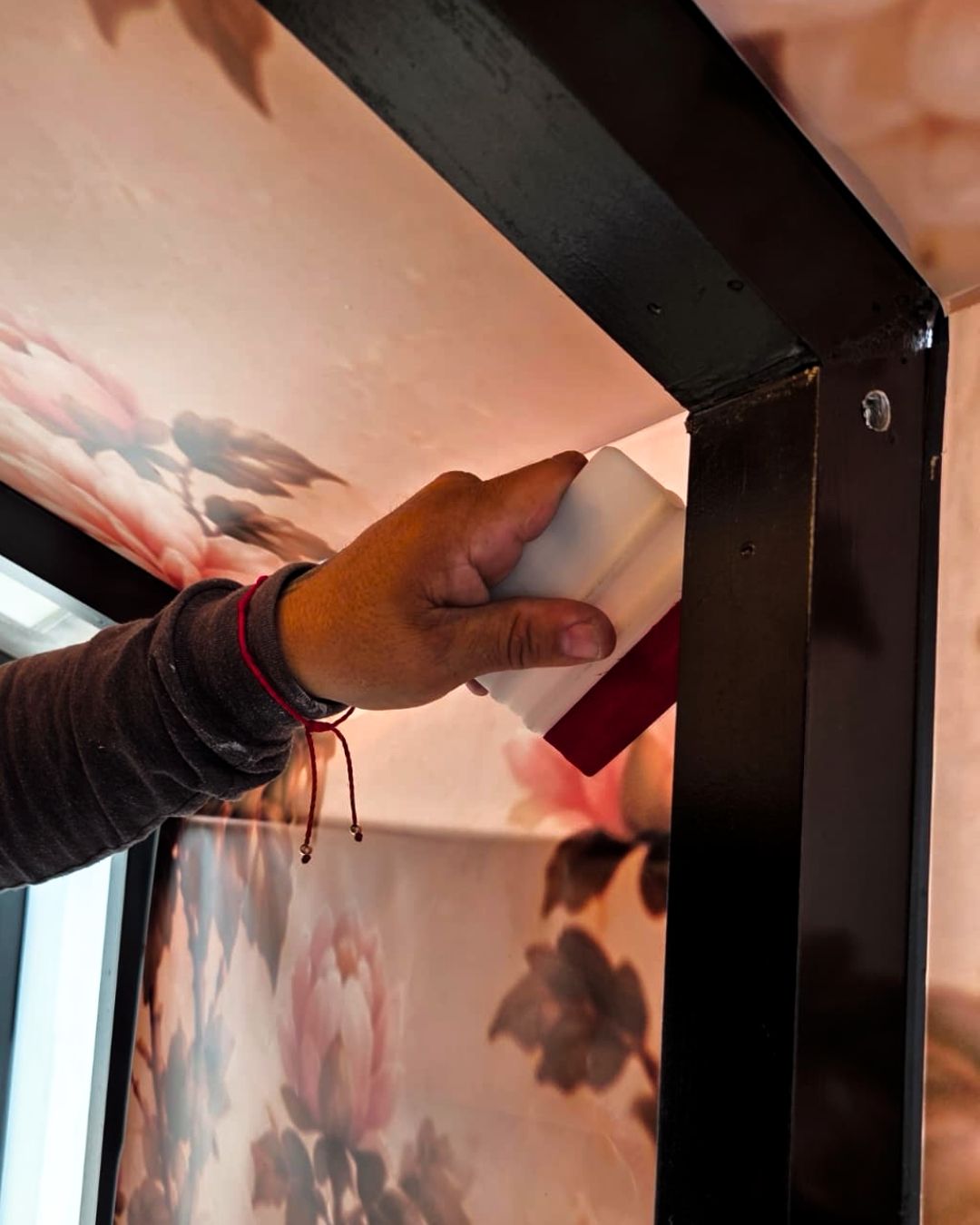Hand holding a small white block beside a black-framed wall panel with cloud wallpaper.