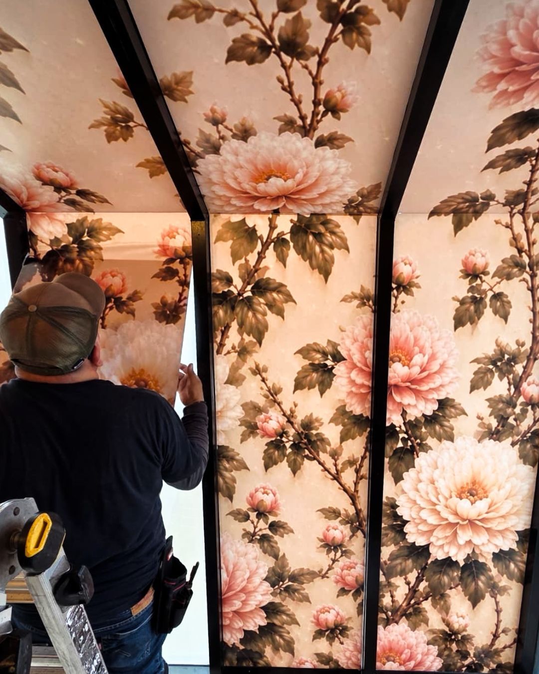 A worker installs floral wallpaper on the ceiling and wall panels.