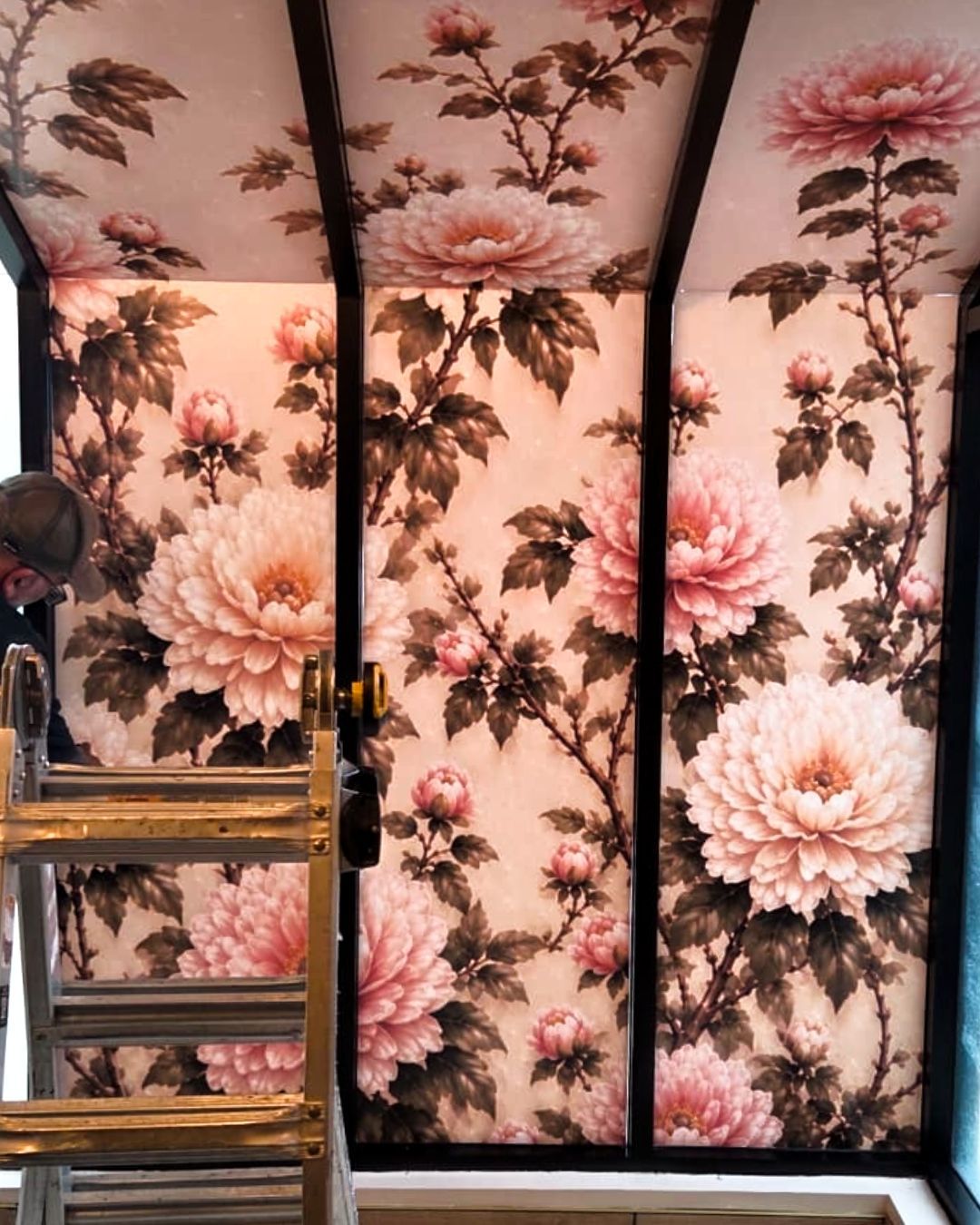 Floral wallpaper panels in pink and black, with a ladder and chair in a room.