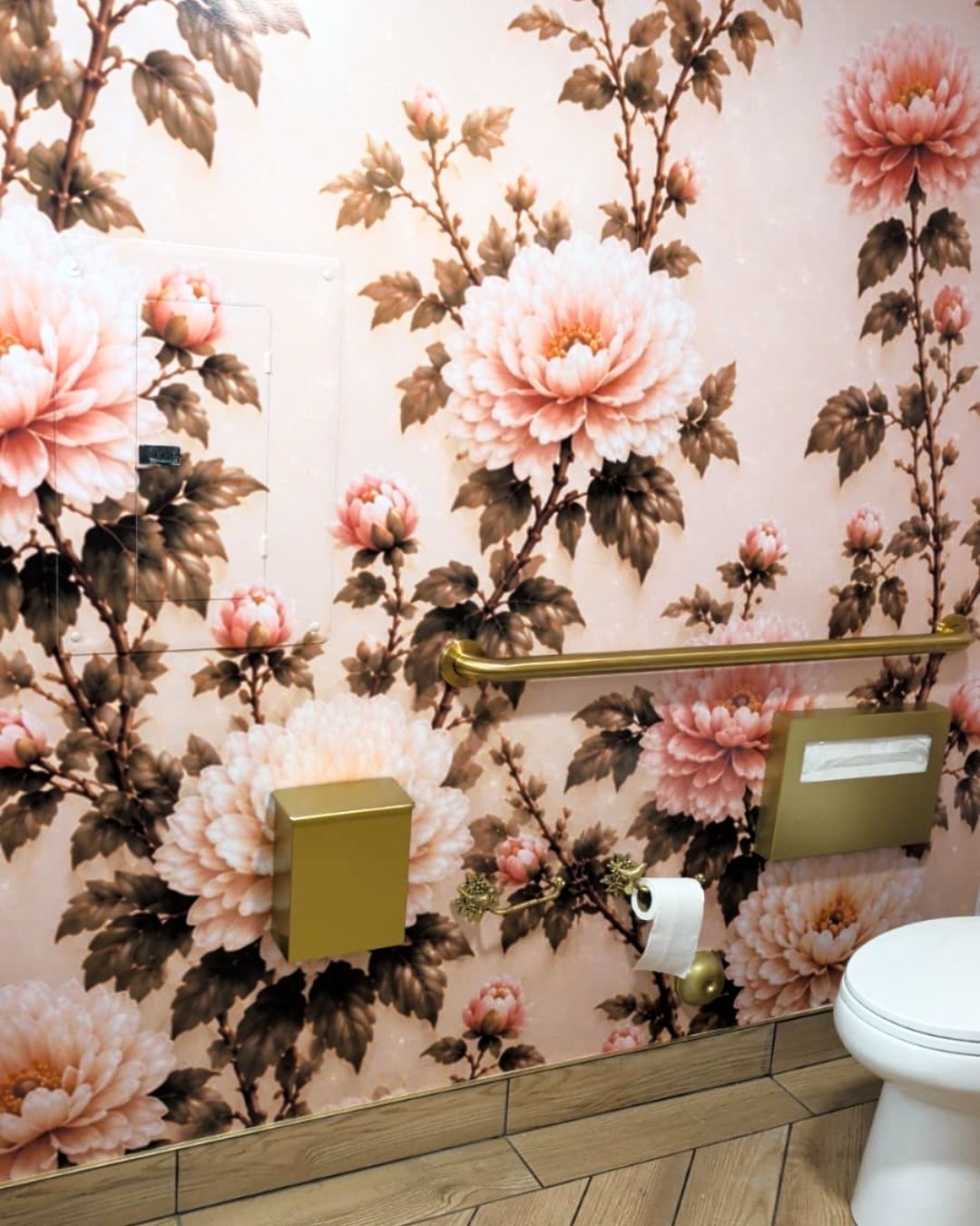 Floral wallpapered bathroom with gold fixtures, toilet, and toilet paper holder.