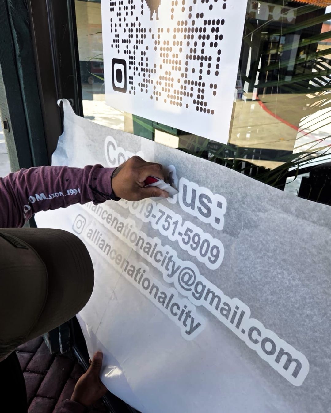 Person applying white lettering to a gray window sign with a phone number and email address