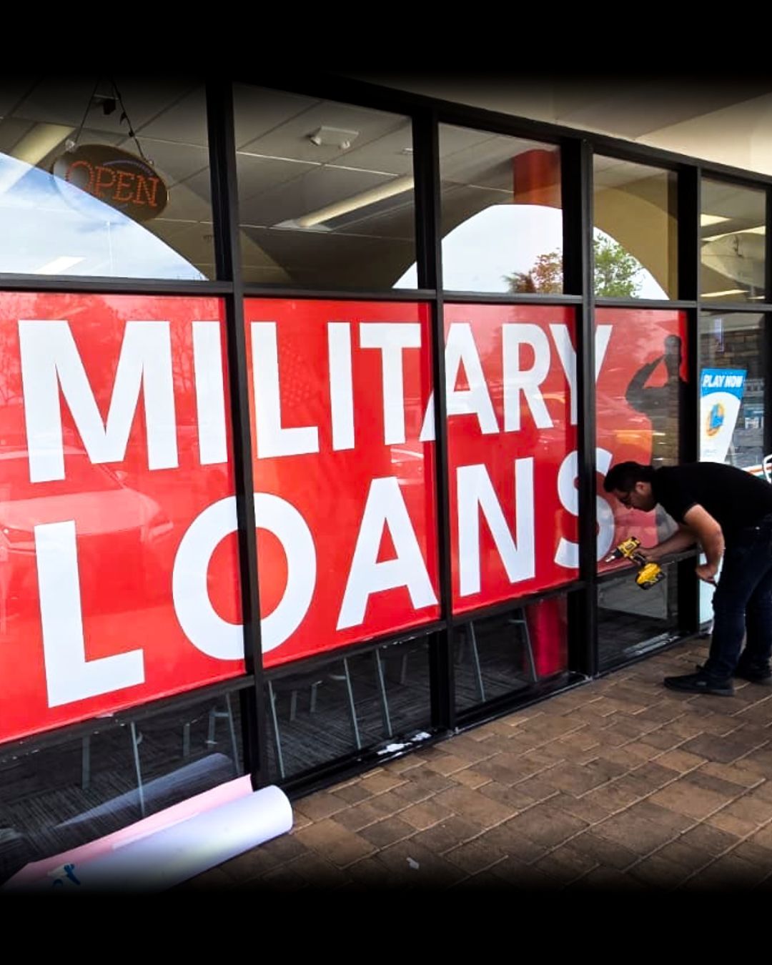 A person installs a large red MILITARY LOANS banner on a storefront window