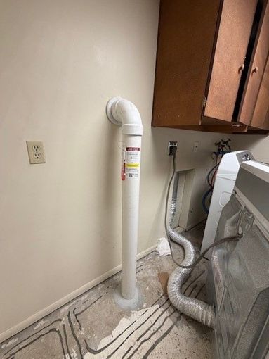 Laundry room with a white vent pipe and flexible dryer hose beside cabinets and a washer.