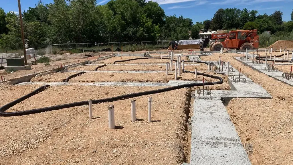 New home foundation site with concrete footings, plumbing pipes, and gravel under construction