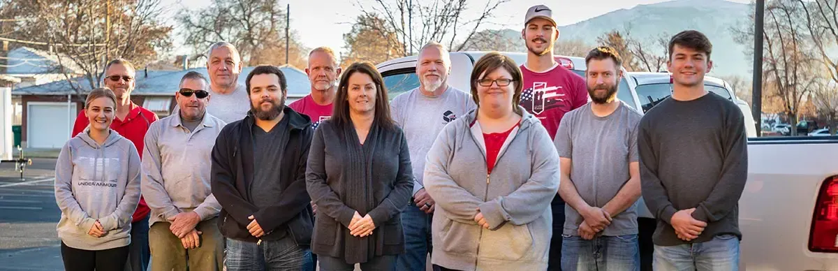 A group of people standing outdoors in front of parked cars, smiling at the camera.