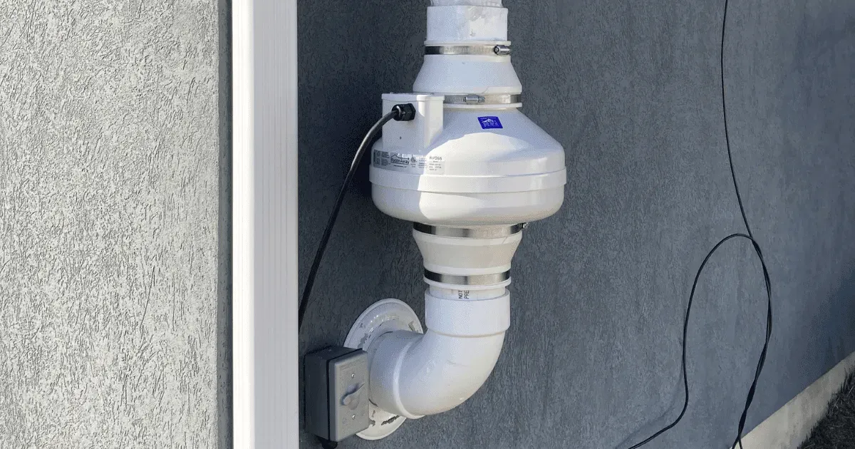 White plumbing vent pipe and meter on a gray exterior wall beside a window frame
