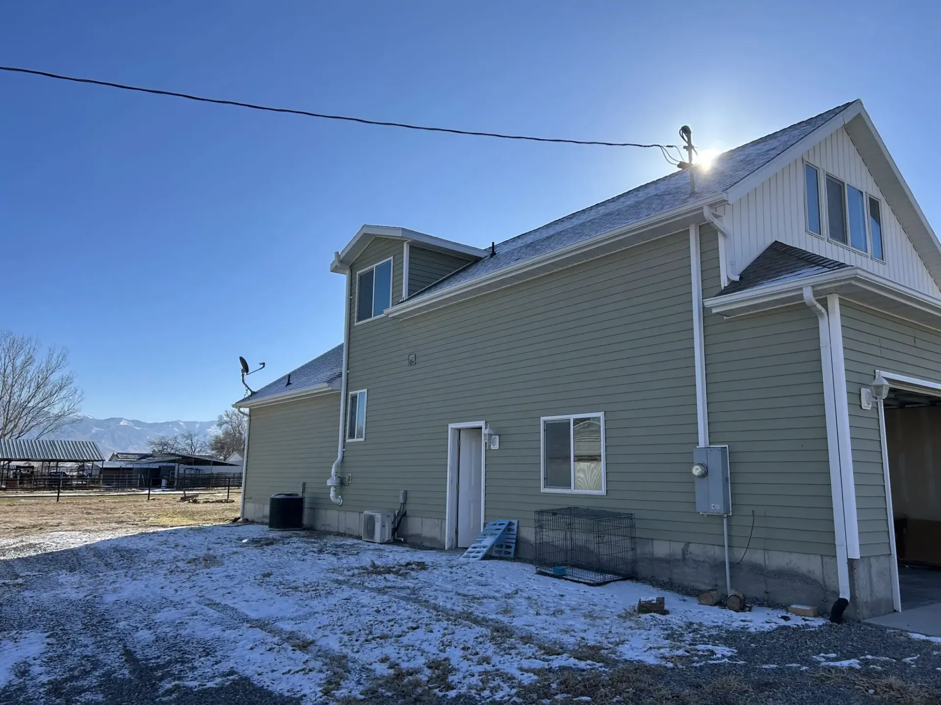 Snow-dusted beige house with white trim under a clear blue sky, viewed from the side.