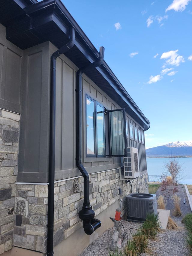 Stone house by a lake with open windows, black rain gutters, and blue sky