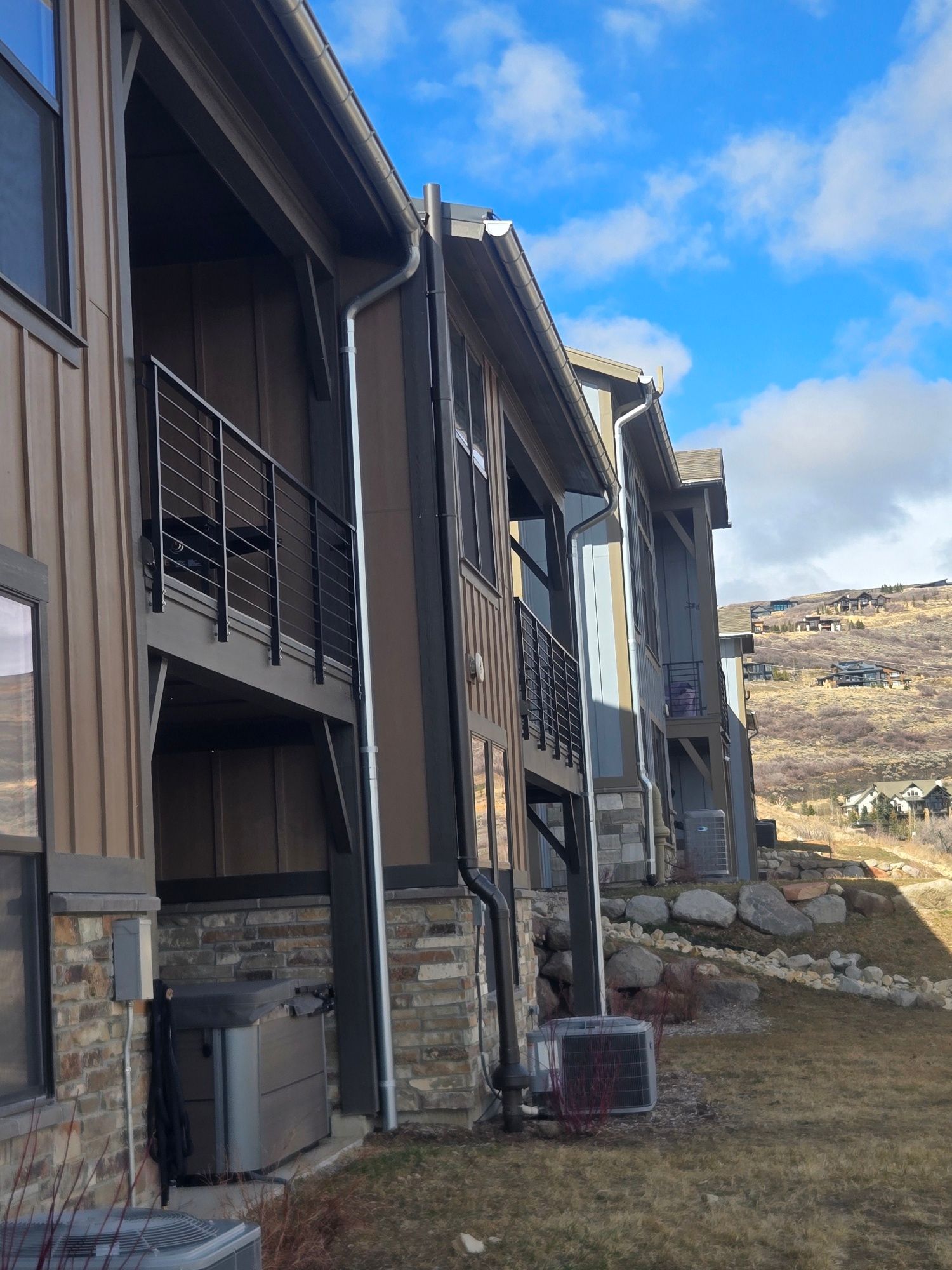 Row of brown townhouses beside a grassy hillside under a blue sky