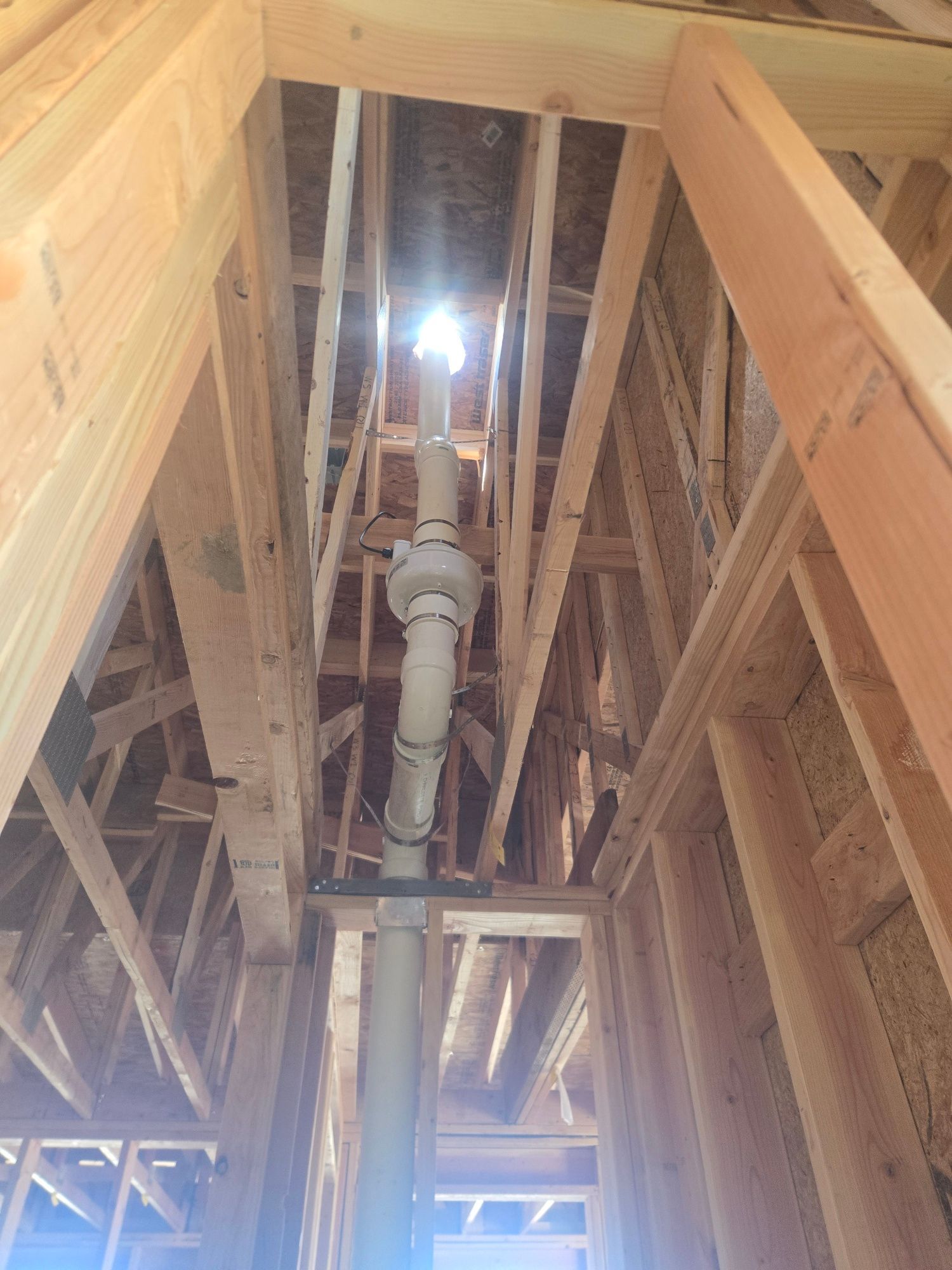 Exposed attic framing with a central white pipe or vent running up to a bright opening above.