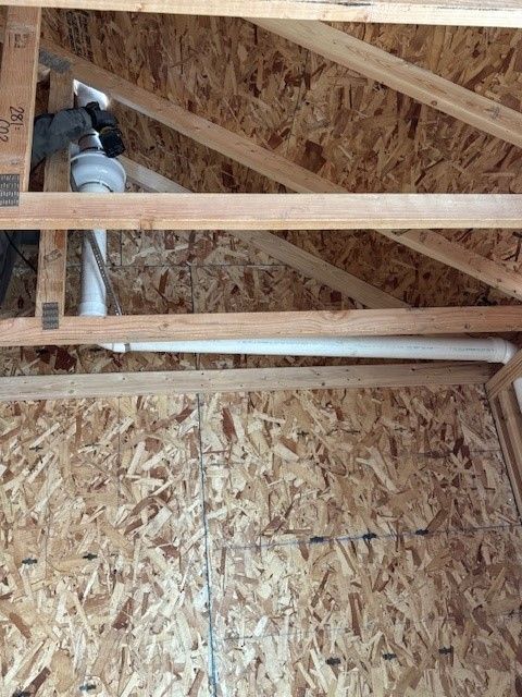 A person in a blue shirt working in an unfinished attic with exposed OSB walls and roof beams.